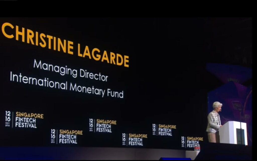 Christine Lagarde at the Singapore Fintech Festival - a man standing at a podium in front of a scree