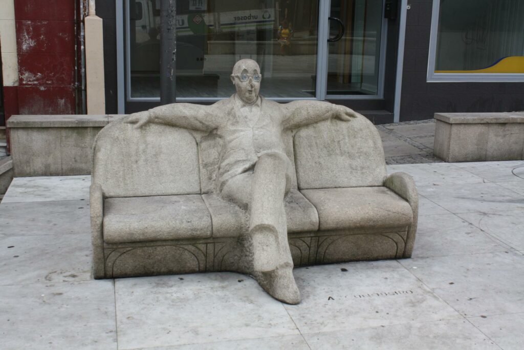 File:Coruña, praza do Humor 01-02a.JPG - a concrete bench with a man sitting on it